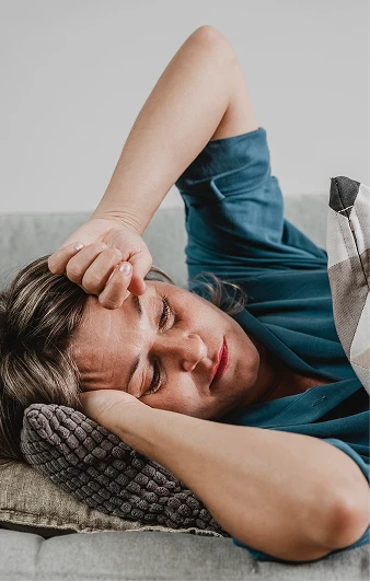 Woman lying on a sofa with a hand against her forehead.